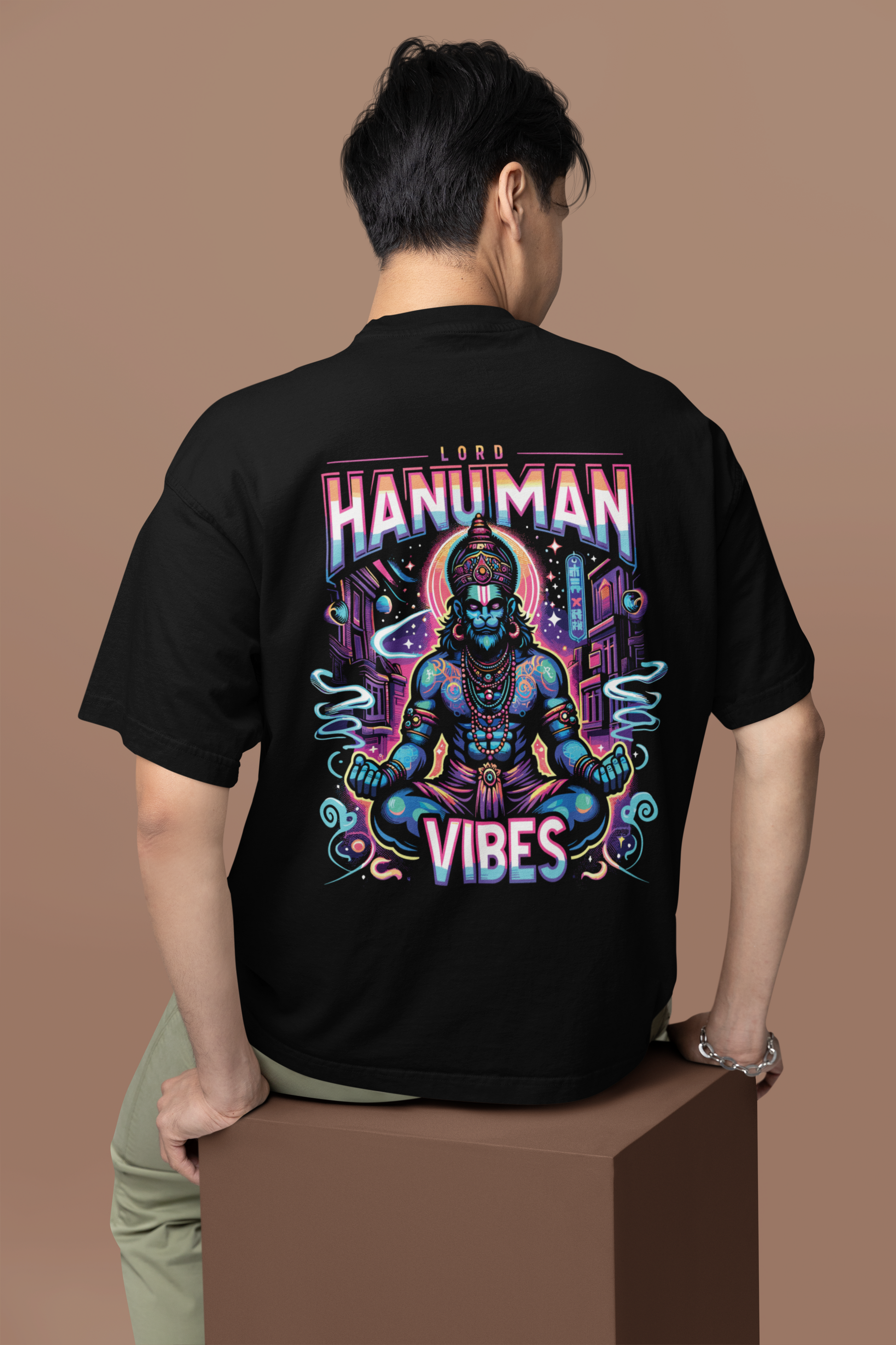 Person wearing a black t-shirt with a colorful 'Hanuman Vibes' design on the back against a brown background