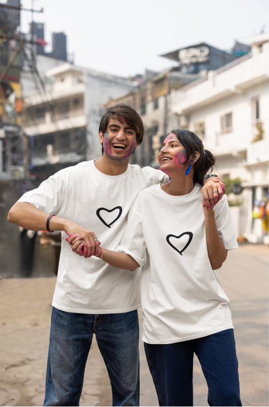 Two people wearing white t-shirts with black hearts, standing on a street.
